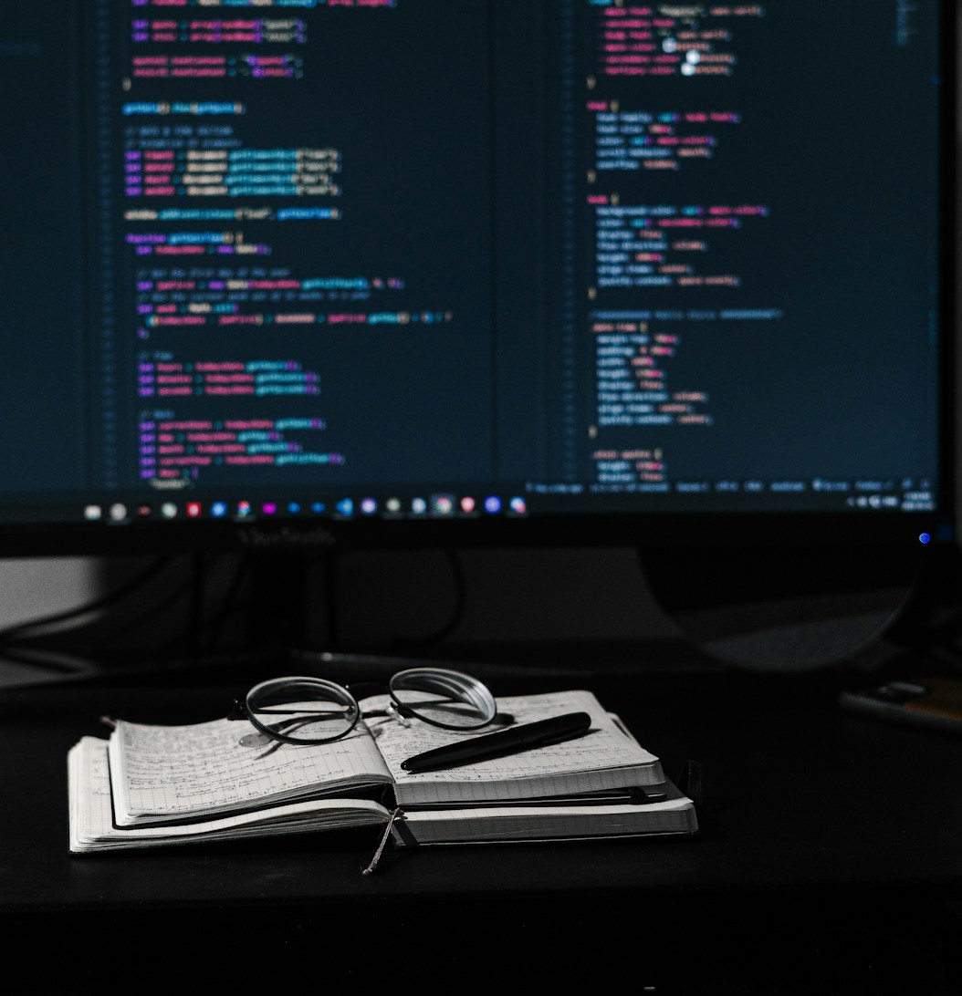 Workspace with computer monitors, notebook, pen, and glasses